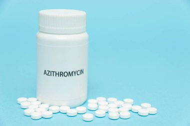 AZITROMYCIN antibiyotiği beyaz şişe ambalajında dağınık haplarla birlikte. COVID-19 tedavisi. Mavi arka planda izole edilmiş. Uzayı kopyala Yakın plan..