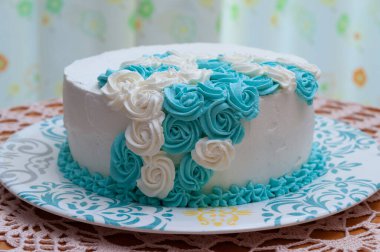 Beyaz ve mavi kremayla süslenmiş doğum günü pastası. Ev yapımı kek yapıyorum. Çiçekli perde arkası. Ön manzara. Yakın plan.. 