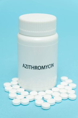 AZITROMYCIN antibiyotiği beyaz şişe ambalajında dağınık haplarla birlikte. COVID-19 tedavisi. Mavi arka planda izole edilmiş. Yakın plan. Dikey çekim.