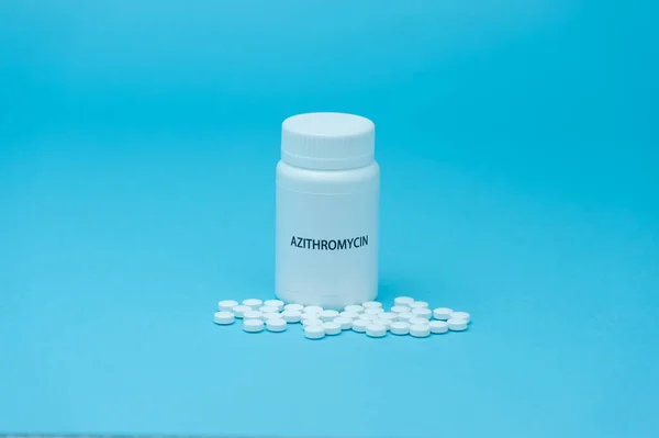 AZITROMYCIN antibiyotiği beyaz şişe ambalajında dağınık haplarla birlikte. COVID-19 tedavisi. Mavi arka planda izole edilmiş. Uzayı kopyala Yatay çekim.