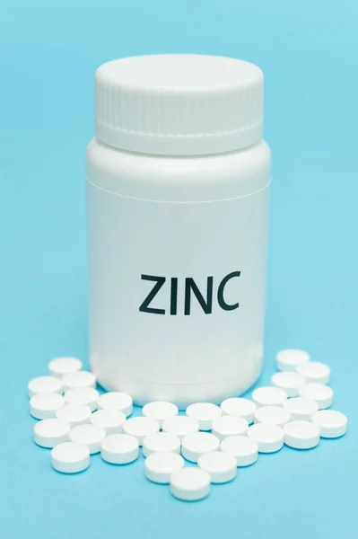 ZINC beyaz şişe ambalajında dağınık haplarla. Besin takviyesi. COVID-19 tedavisi. Mavi arka planda izole edilmiş. Yakın plan. Dikey çekim.