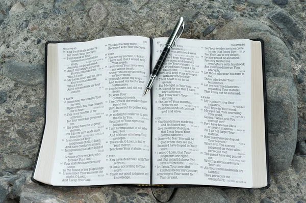 Open bible in Psalm 119 with a fountain pen. Stone background.