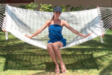 Hamakta dinlenen beyaz şapkalı bir kadın tatilde güneşleniyor.