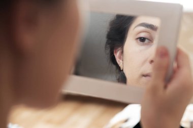 aynaya bakarak kendini makyaj yapıyor kız