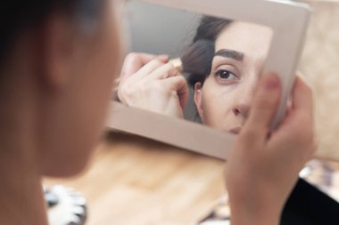 aynaya bakarak kendini makyaj yapıyor kız