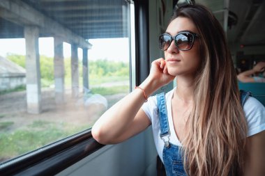 Trende güneş gözlüğü takan genç bir kız pencereden dışarı bakıyor. Yolculukta iyi bir ruh hali