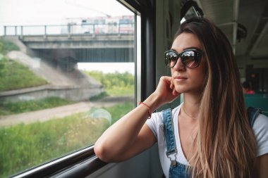 Trende güneş gözlüğü takan genç bir kız pencereden dışarı bakıyor. Yolculukta iyi bir ruh hali