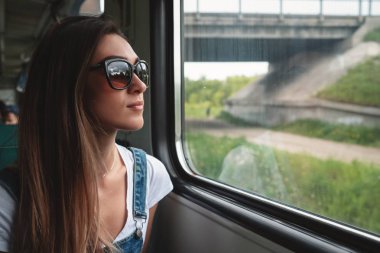 Trende güneş gözlüğü takan genç bir kız pencereden dışarı bakıyor. Yolculukta iyi bir ruh hali