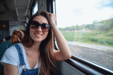 Trende güneş gözlüğü takan genç bir kız pencereden dışarı bakıyor. Yolculukta iyi bir ruh hali