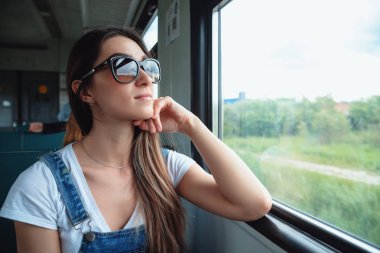 Trende güneş gözlüğü takan genç bir kız pencereden dışarı bakıyor. Yolculukta iyi bir ruh hali