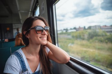Trende güneş gözlüğü takan genç bir kız pencereden dışarı bakıyor. Yolculukta iyi bir ruh hali