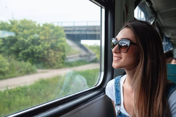 Trende güneş gözlüğü takan genç bir kız pencereden dışarı bakıyor. Yolculukta iyi bir ruh hali