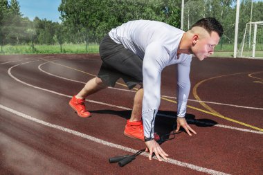 Genç kaslı sporcu stadyumdaki koşu bandının başında.