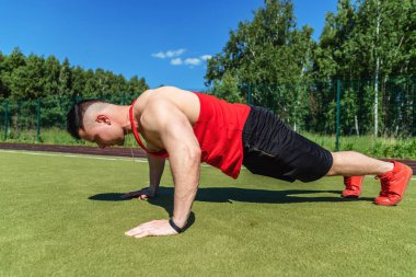 Genç bir atlet sıcak bir yaz gününde bir spor stadyumunda şınav yapıyor.