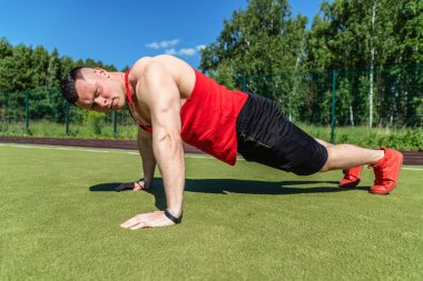 Genç bir atlet sıcak bir yaz gününde bir spor stadyumunda şınav yapıyor.