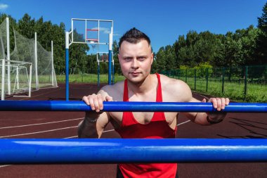 Spor stadyumundaki genç çalıştırıcı yatay bara yaslandı ve kameraya baktı.