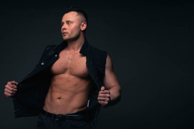 Kasları ve pazıları olan güçlü ve yakışıklı genç bir adam. Siyah arkaplanda stüdyo çekimi