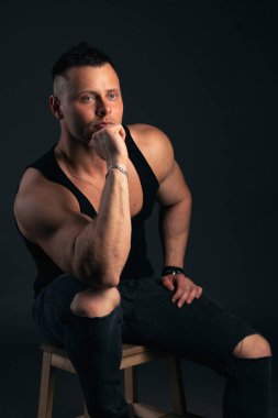 Kasları ve pazıları olan güçlü ve yakışıklı genç bir adam. Siyah arkaplanda stüdyo çekimi