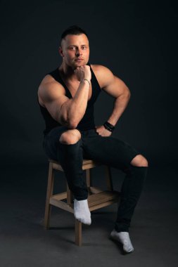 Kasları ve pazıları olan güçlü ve yakışıklı genç bir adam. Siyah arkaplanda stüdyo çekimi