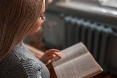 Kız masada oturuyor ve bir kitap okuyor.