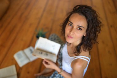 Kitapları olan kıvırcık saçlı bir kız ahşap zeminde oturuyor. Uzaklık öğrenimi