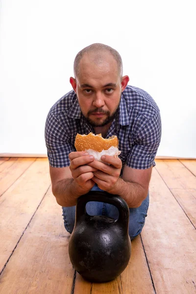 男はハンバーガーと木製の床に体重で座っています 健康的なライフスタイルの概念 — ストック写真