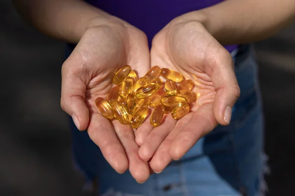A handful of vitamin d capsules are in women\'s hands. Blurred background