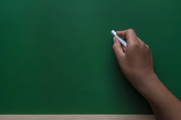 African american woman hand writing with white chalk on a green chalkboard