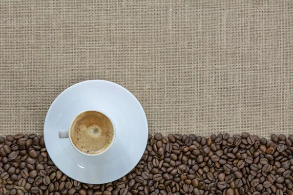 cup of coffee on a frame of coffee beans on a texture of a burlap background