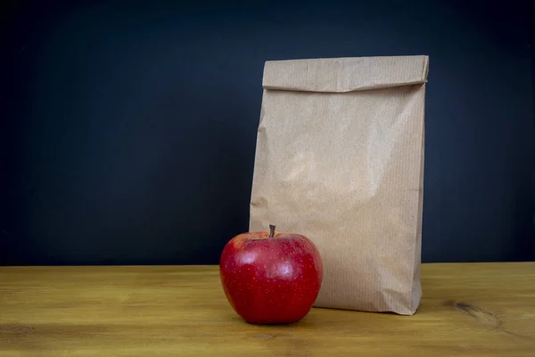 School lunch. Brown paper bag and a red apple on top of wooden desk