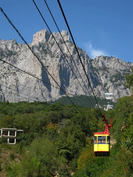 Koncepce cestování a cestovního ruchu. Žluté Lanky šplhá vysoko na horu. krajina s lanovkou — Stock fotografie