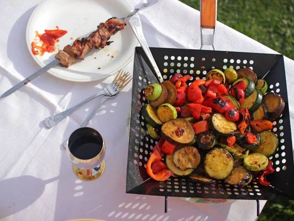 Sebze dilim, barbekü bir tabak ve dışında beyaz masada bir fincan şarap ile kızartma tavası