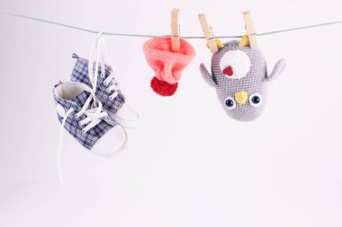 El yapımı bir oyuncakla güzel bir bebek sahnesi. Tığ işi Amigurumi penguen oyuncağı ve bebek ayakkabıları beyaz arka planda çamaşır ipinde asılı duruyor. Dünya örgü günü konsepti..