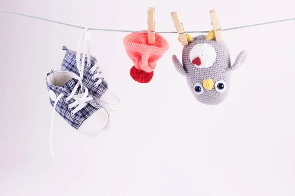 El yapımı bir oyuncakla güzel bir bebek sahnesi. Tığ işi Amigurumi penguen oyuncağı ve bebek ayakkabıları beyaz arka planda çamaşır ipinde asılı duruyor. Dünya örgü günü konsepti..