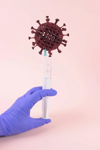 Salgın covid19 konsepti. Mavi tıbbi eldiven verin. Pembe arka planda 3 boyutlu koronavirüs izole ve bulanık şırınga ile. Hastalığı durdurma, salgını durdurma sembolü. Kopya uzayı