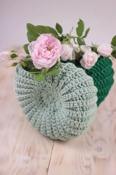Pink shrub rose in crochet light green basket close up on wooden table. Handmade decoration,handy crafts, hobby activity — Stock Photo, Image