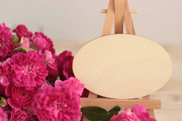 Küçük ahşap sehpanın üzerinde tahta oval plaket pembe gül arka planı üzerinde. Boş boş tahta çerçeve tasarım veya metin için kullanılabilir..