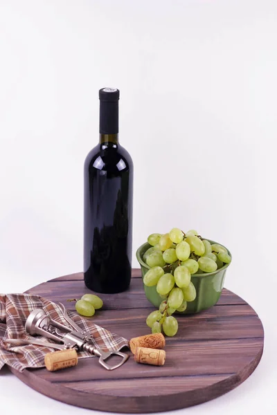 Weinflasche und Trauben auf einem alten Weinfass Draufsicht aus nächster Nähe. Wein-Accessoires auf dunklem Holz runden Teller isoliert.Weißer Hintergrund. — Stockfoto
