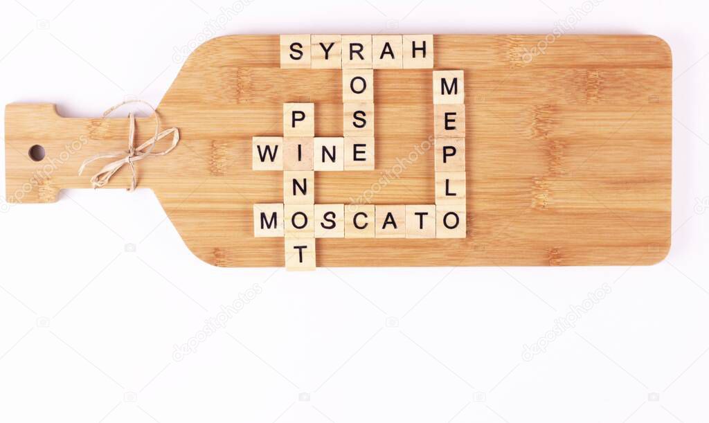 variety of wines listed in the crossword on handmade cutting board.wines name on wooden cubes.kitchen wooden board on white background.