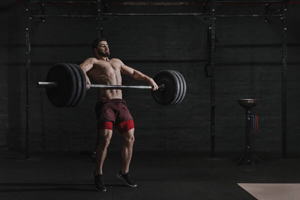 Muscular man lifting a barbell in crossfit gym.