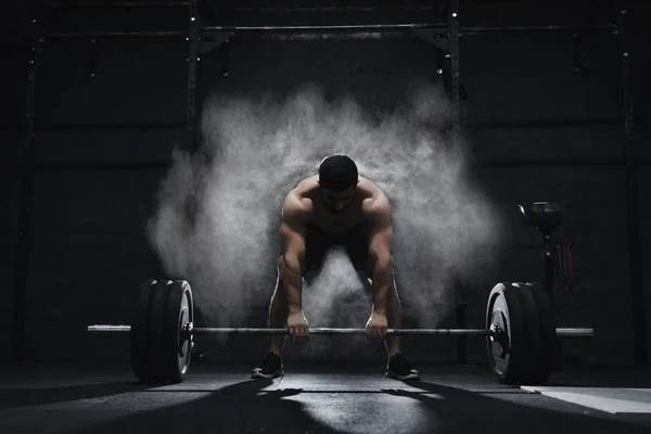 Crossfit atlet spor toz bulutu içinde ağır halter kaldırmaya hazırlanıyor. Halter magnesia koruma.