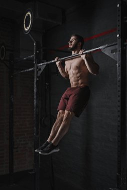 Young crossfit athlete doing pull-ups at the gym. Strong man doing functional training. Workout exercises. Calisthenics practicing clipart