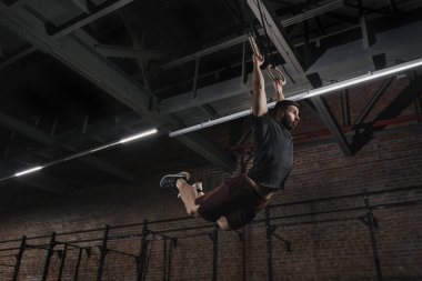 Genç atlet pull-up çapraz uygun spor salonu jimnastik halkaları üzerinde yapıyor. Yakışıklı adam kas pratik sallanan egzersiz egzersiz ups.