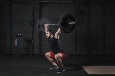 Genç fit atlet barbell ile ağız kavgası yaparken başının üzerine çapraz. Fonksiyonel eğitim pratik adam. Powerlifting Egzersiz Egzersizler
