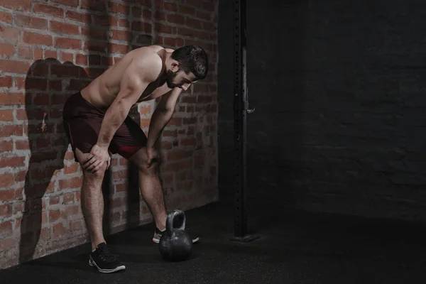 Athlete is leaning against the wall at the gym suffering breakdown to overcome. Demotivation sport concept. Stress and fatigue in sport. Crossfit kettlebell training. Copy space.