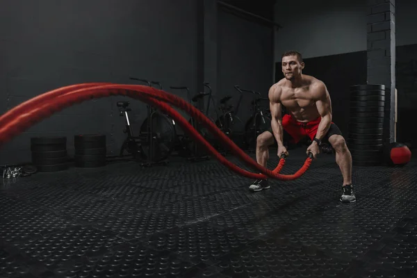 Muž nosí červené kraťasy dělat bitvu lana cvičení na crossfit — Stock fotografie