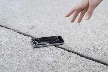Young woman pick up her broken smartphone with cracked screen gl