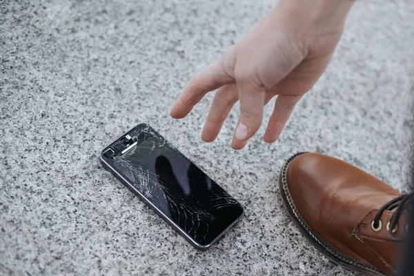 Young woman picks up her broken smartphone with cracked screen g