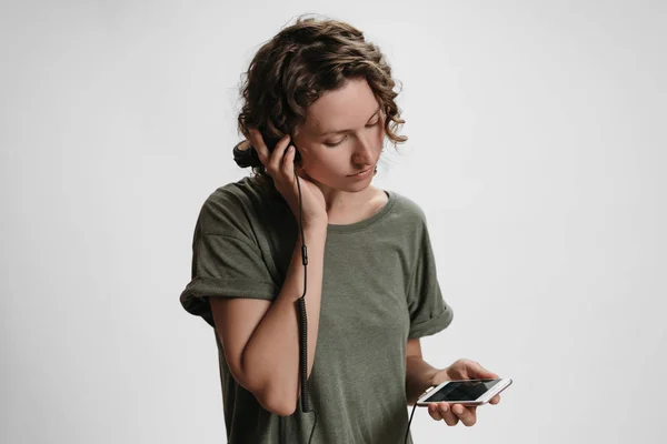 Ung lockig kvinna fritid, hålla hennes moderna stereo hörlurar — Stockfoto