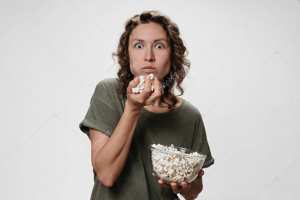 Young woman with curly hair eating popcorn, watching a movie or 